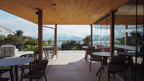 A covered outdoor seating area with tables and chairs, overlooking a mountainous landscape. - Siramat Hotel (Petrópolis)