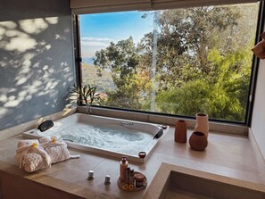 Ein Badezimmer mit Badewanne, Handtüchern, Pflegeprodukten und Blick ins Grüne durch ein Fenster.
