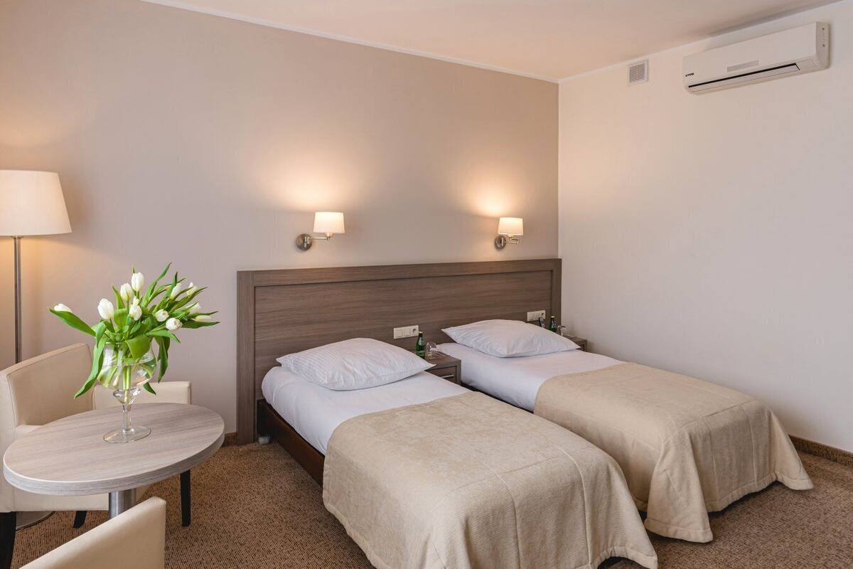 Una habitación de hotel con dos camas, una mesita y un florero, y una lámpara.