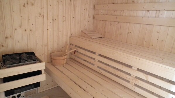 A sauna with wooden benches and a bucket of rocks.