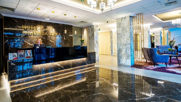 A hotel reception area with a marble counter, a chandelier, and a seating area with a blue chair and a small table. - Hotel Gromada Koszalin (Koszalin)