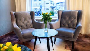 Two armchairs facing each other with a small round table between them, a vase with yellow flowers on the table, and a view of buildings through a window. - Hotel Gromada Koszalin (Koszalin)