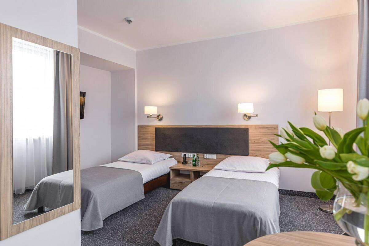 Habitación de hotel con dos camas, una mesita pequeña, un espejo y una mesita de noche con lámpara.