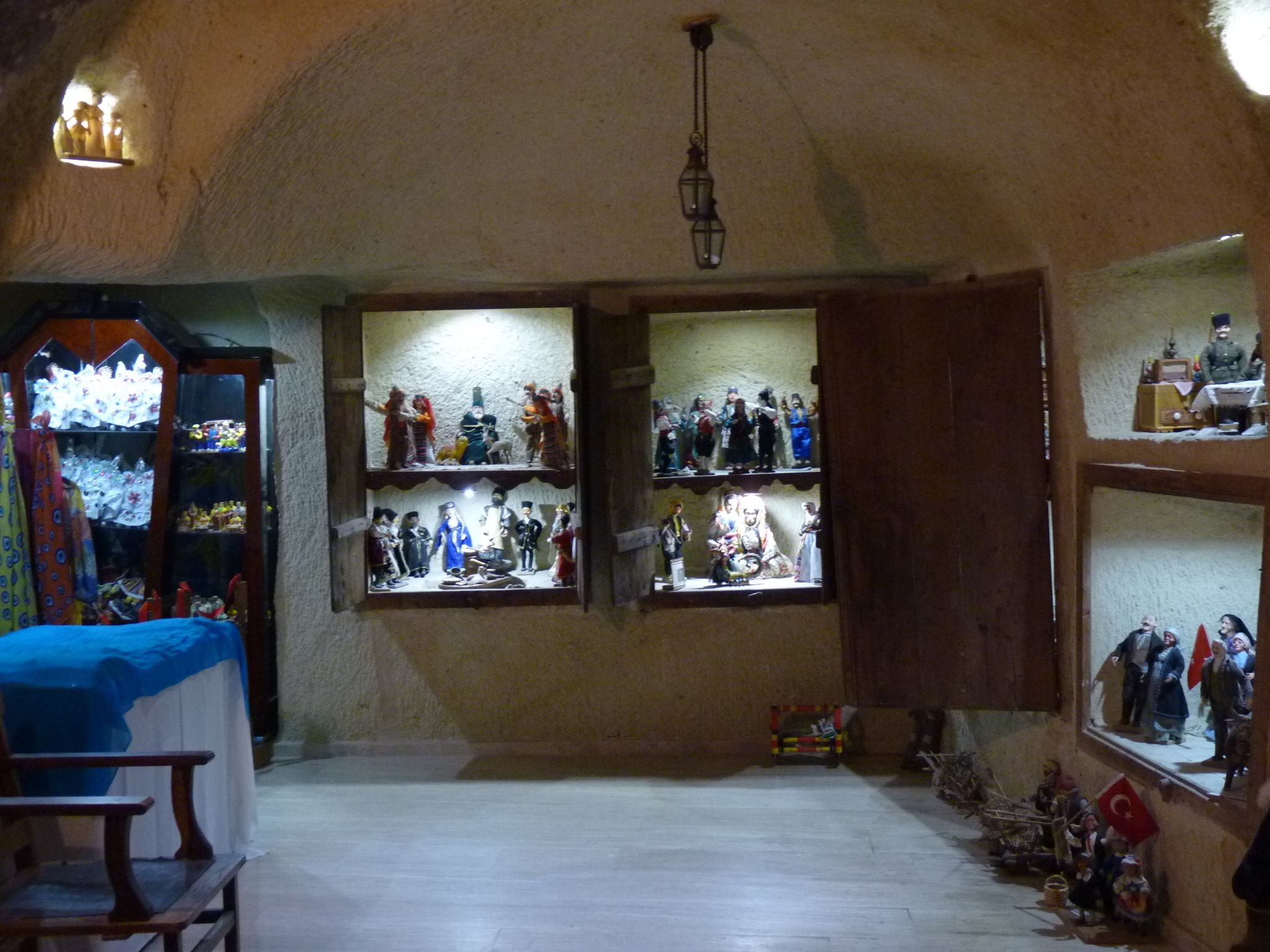 Une pièce dotée d’un plafond voûté et d ’une hauteur impressionnante, ainsi que de poutres en bois. Deux fenêtres, ornées d’étagères où sont exposées des figurines, s’y trouvent. Un banc en bois est adossé au mur, et une petite table avec une lampe se trouve au centre de la pièce.