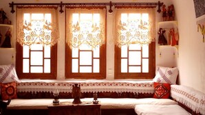 A traditional room with a sofa set, a small table, and three windows with lace curtains. - Buyuk Sinasos Konagi (Ürgüp)