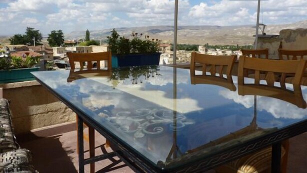 A glass-top table with wooden chairs, a potted plant, and a view of a town and mountains. - Buyuk Sinasos Konagi (Ürgüp)