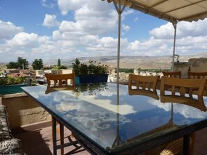 A glass-top table with wooden chairs, a potted plant, and a view of a town and mountains.