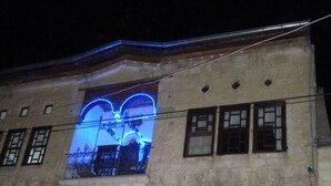 A historic building with a large illuminated archway entrance, a mural on the lower wall, and a sign indicating it is the Cappadocia Art History Museum. - Buyuk Sinasos Konagi (Ürgüp)