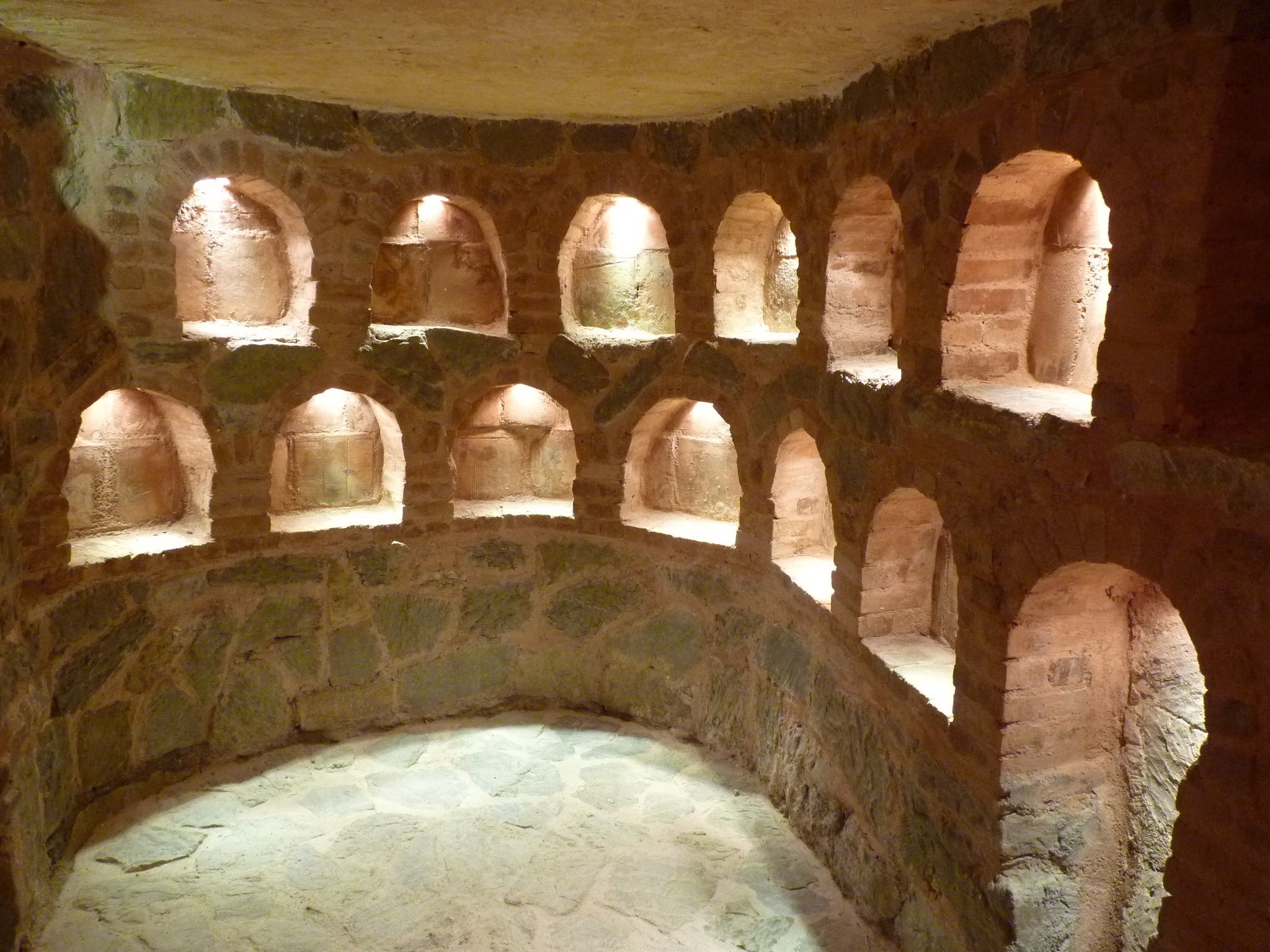 Una habitació de parets de pedra amb diverses finestres d'arc i un banc de pedra al centre.