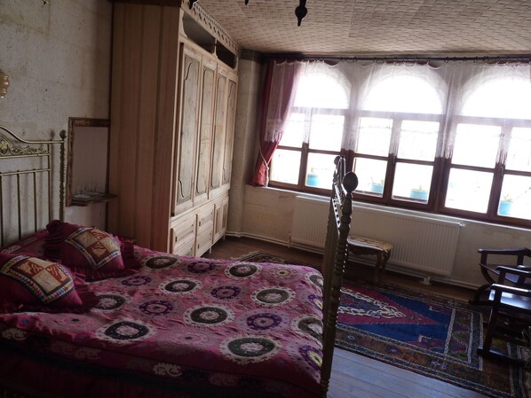 A bedroom with a four-poster bed, a wooden wardrobe, a small table, and a window with curtains.