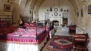 A room with a large bed, a fireplace, and a stone archway. - Buyuk Sinasos Konagi (Ürgüp)