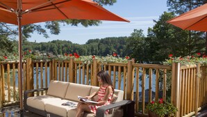 Eine Frau sitzt auf einem beigen Sofa und blickt auf einen See, mit einem Holzdeck und einem Holzzaun im Hintergrund.