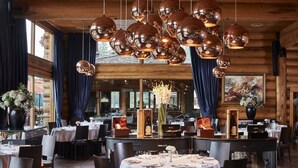 Ein Restaurant mit runden Tischen, dunklen Vorhängen und hängenden Kupferlüstern.