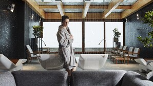 Ein moderner Wellnessraum mit einer großen Badewanne, einer Sitzecke und bodentiefen Fenstern.