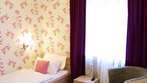 Une chambre à coucher avec un lit, une table de chevet, une chaise et une fenêtre avec des rideaux.
