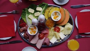 Un plateau de petit-déjeuner comprenant divers fromages, charcuteries, fruits et confitures, présenté sur un plateau en argent.