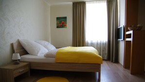 Une chambre à coucher avec un lit, une table de chevet, un tapis jaune, un tableau accroché au mur et un téléviseur fixé au mur.