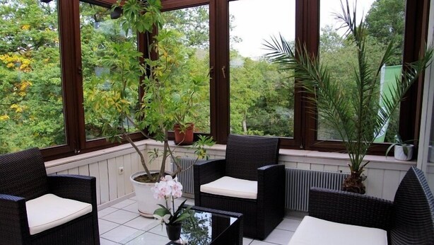 Une véranda avec des meubles en osier, de grandes fenêtres et des plantes en pot.