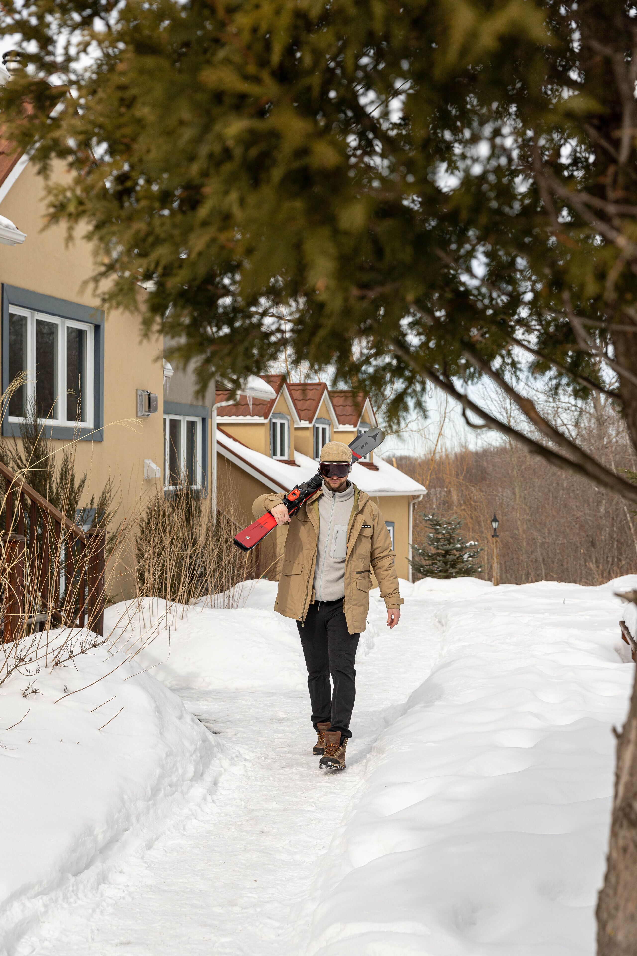 Una persona caminando por un sendero cubierto de nieve hacia una casa con techo nevado y una ventana de marco blanco.