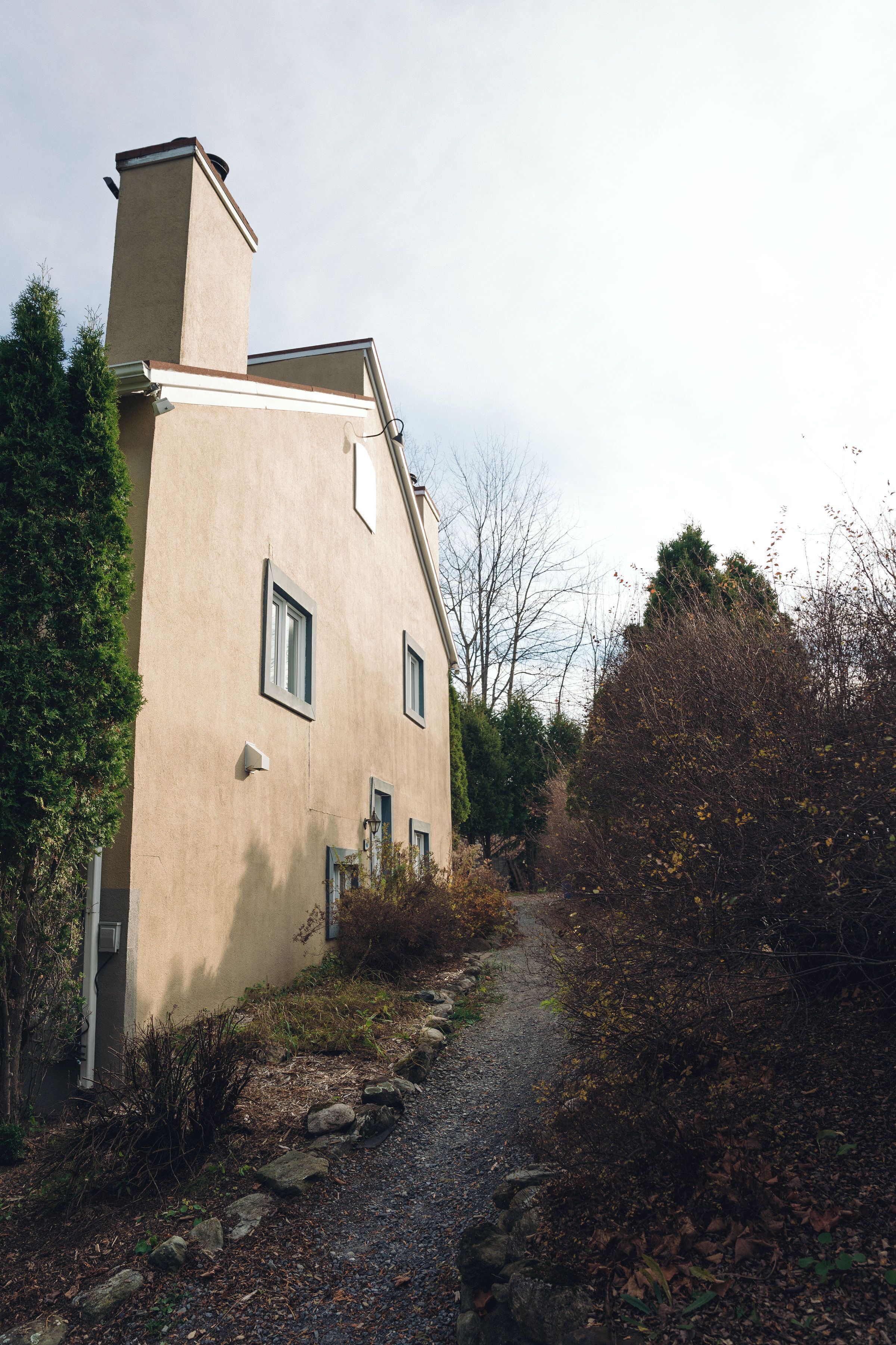 Ein zweistöckiges Gebäude mit sandfarbener Fassade, einem Schornstein und einem Weg zum Eingang.
