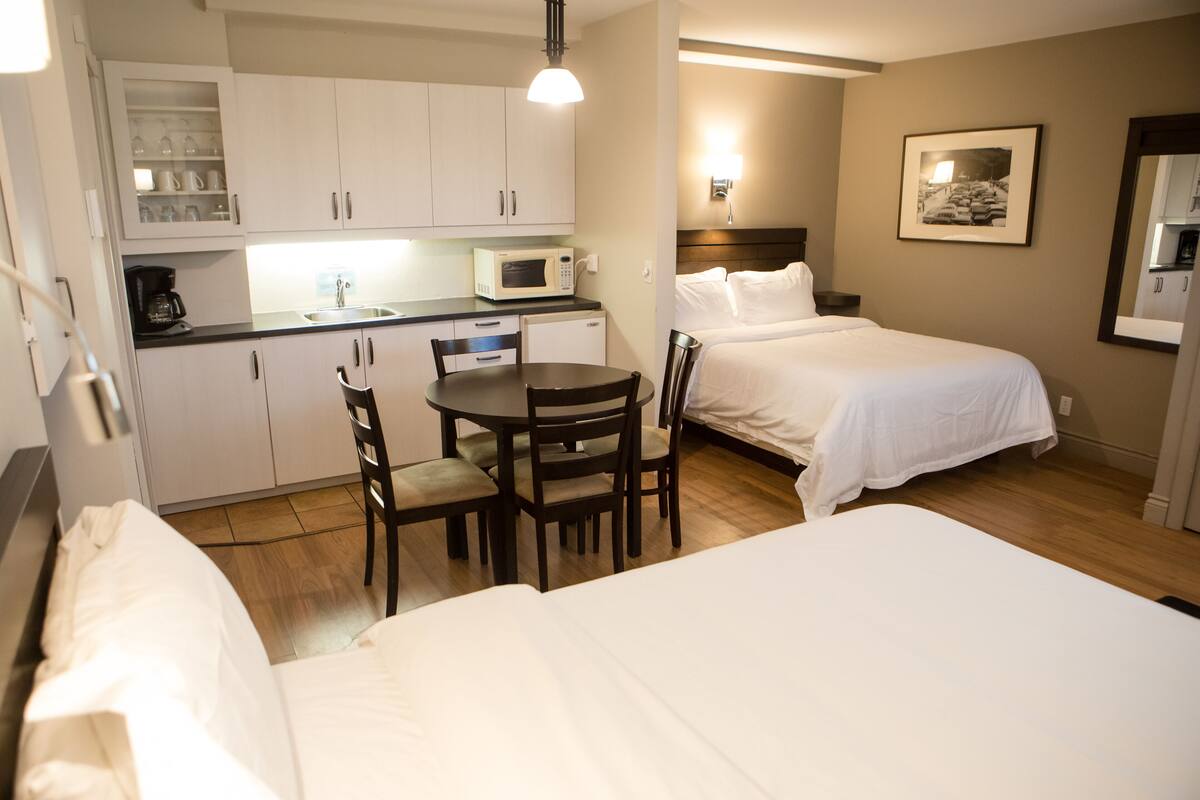 Ein Hotelzimmer mit einer Küchenzeile, einem Esstisch mit Stühlen, einem Bett und einem Nachttisch.