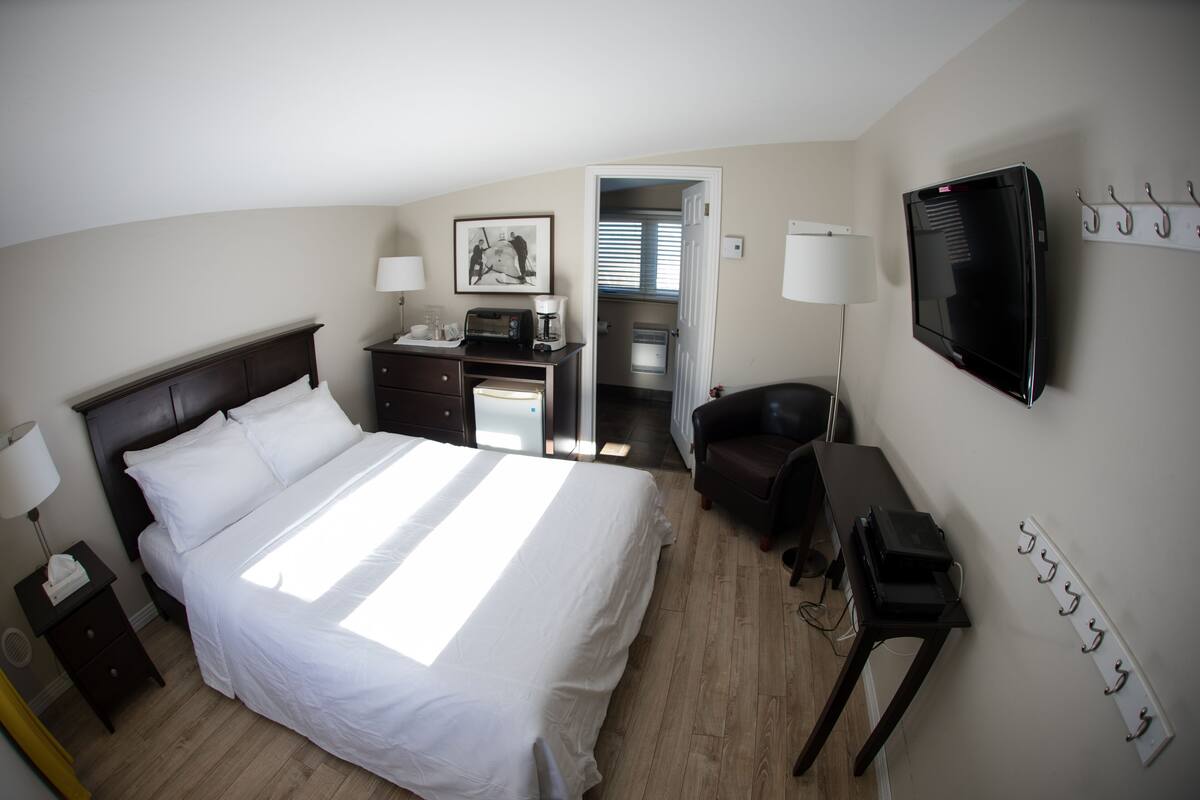 Ein Hotelzimmer mit einem großen Bett, einem Schreibtisch mit Computer, einem Fernseher und einem Kleiderständer.