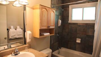 Une salle de bain comprenant un lavabo, un miroir, un meuble en bois, un porte-serviettes, une douche et une fenêtre.