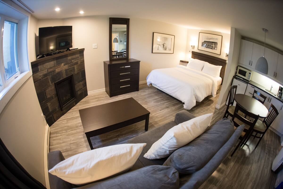 Ein modernes Hotelzimmer mit Kamin, einem Bett, einer Couch, einem Essbereich und einer Küchenzeile.