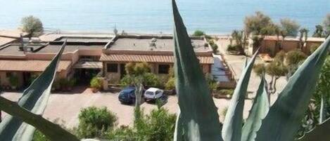 A coastal building with a flat roof, surrounded by vegetation and parked cars.