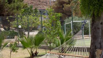 A hammock suspended between trees in a fenced enclosure with a view of a hill and a building in the background.