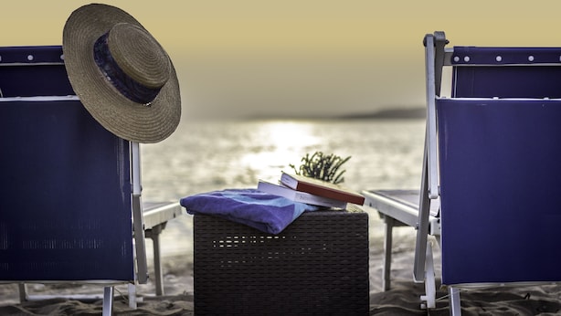 Twee strandstoelen met een rieten mand en een hoed daartussen, met uitzicht op zee.