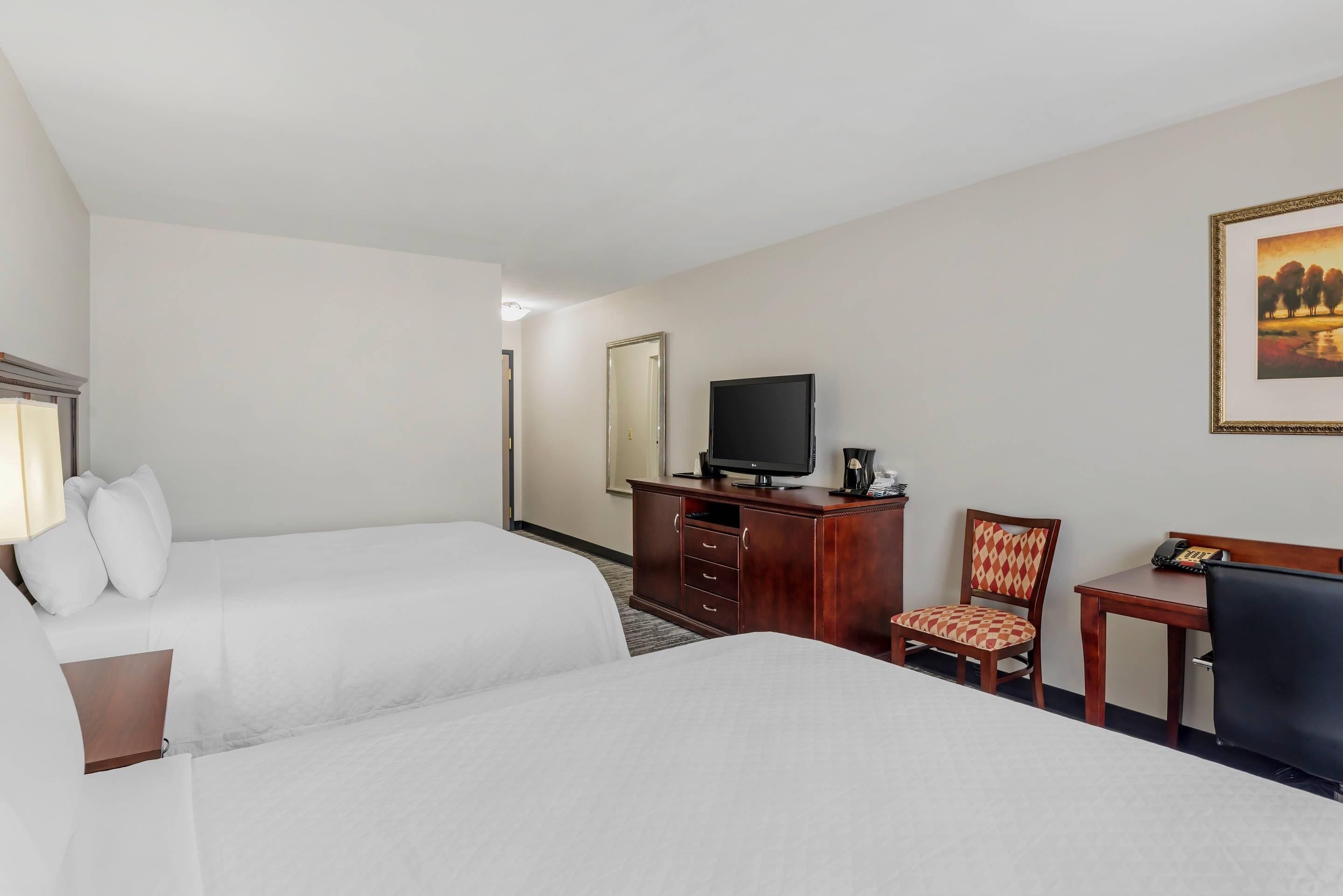 Una habitación de hotel con dos camas, un televisor, un escritorio con una silla y un cuadro en la pared.