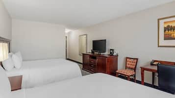 Una habitación de hotel con dos camas, un televisor, un escritorio con una silla y un cuadro en la pared.