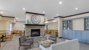 A spacious lounge area with a stone fireplace, seating arrangements, and a large clock on the wall. - Country Inn & Suites by Radisson, Ashland - Hanover, VA (Ashland)