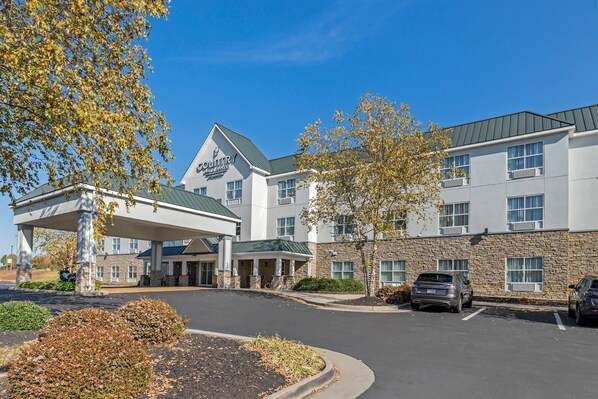 A hotel with a covered entrance, a stone facade, and a parking area.