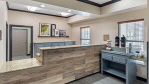 A reception desk with a wooden panel design, a counter with a welcome sign, and a window with blinds. - Country Inn & Suites by Radisson, Ashland - Hanover, VA (Ashland)