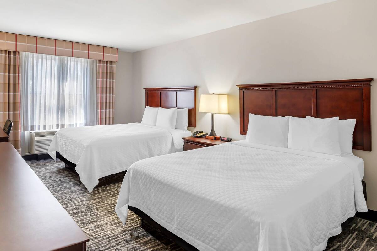 A hotel room with two beds, a desk, a lamp, and a window with curtains.
