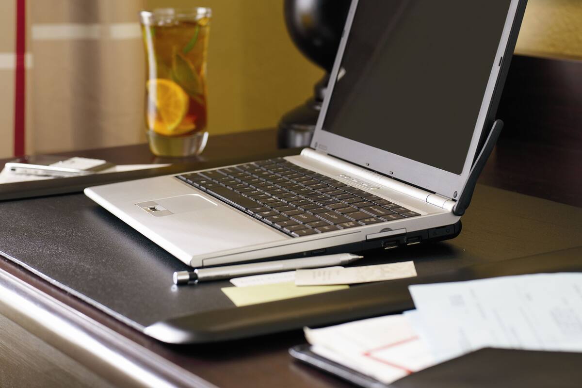 A laptop on a desk with a glass of iced tea, a lamp, and papers.