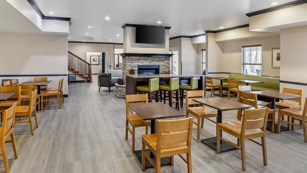 A spacious dining area with multiple tables and chairs, a stone fireplace, and a flat-screen TV mounted above it. - Country Inn & Suites by Radisson, Ashland - Hanover, VA (Ashland)