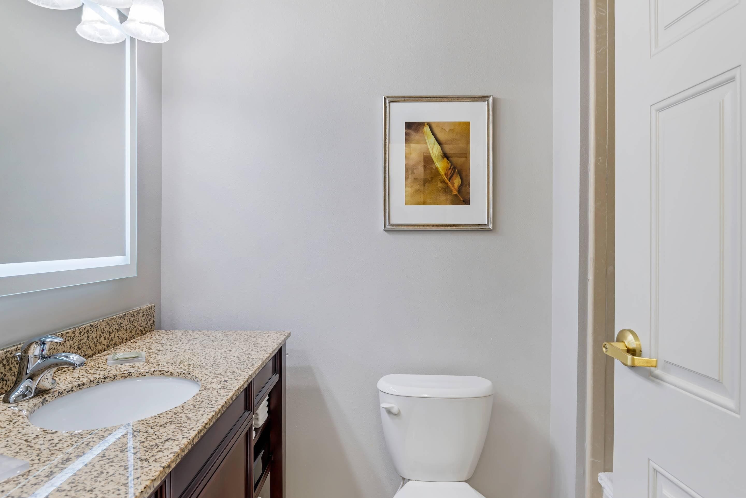 Un baño con lavabo, espejo, inodoro y una obra de arte en la pared.