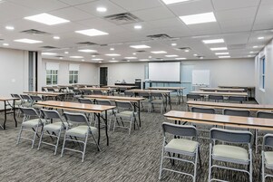 Un aula con escritorios, sillas, una pantalla de proyector y una pizarra.