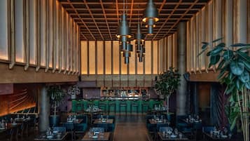A spacious restaurant with high ceilings, multiple hanging pendant lights, and a central bar area.