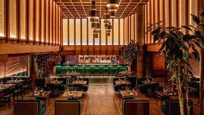 Un restaurante espacioso con techo alto, varias lámparas colgantes y una barra de bar al fondo.