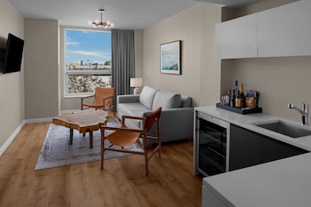 A hotel room with two beds, a large window with curtains, a hanging light fixture, and a view of the cityscape. at CODA Williamsburg