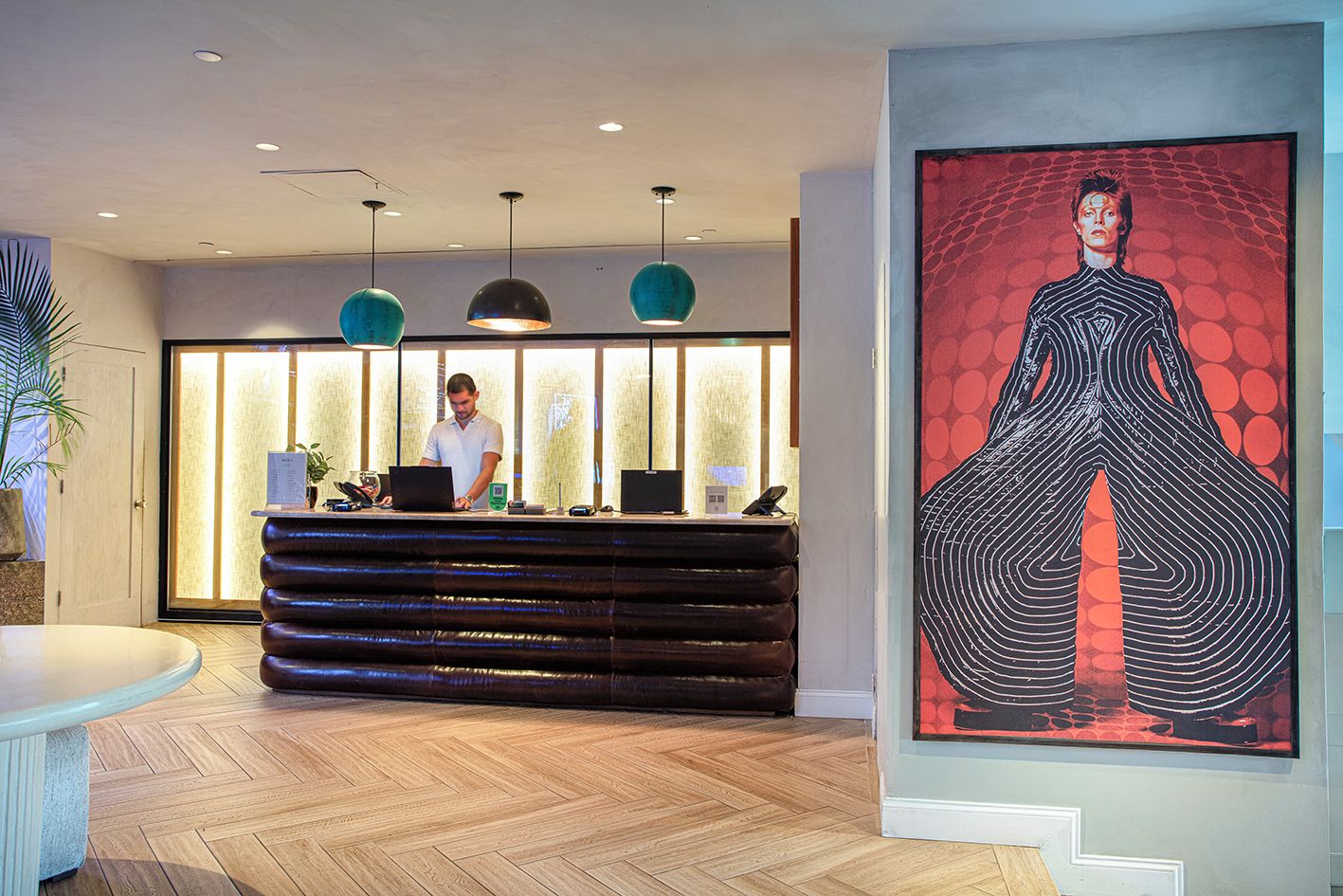A reception desk with a receptionist, a modern pendant light fixture, and a large abstract painting on the wall.