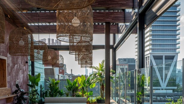 Un moderno espacio de salón con lámparas colgantes de mimbre, asientos cómodos y grandes ventanales con vistas a la ciudad.
