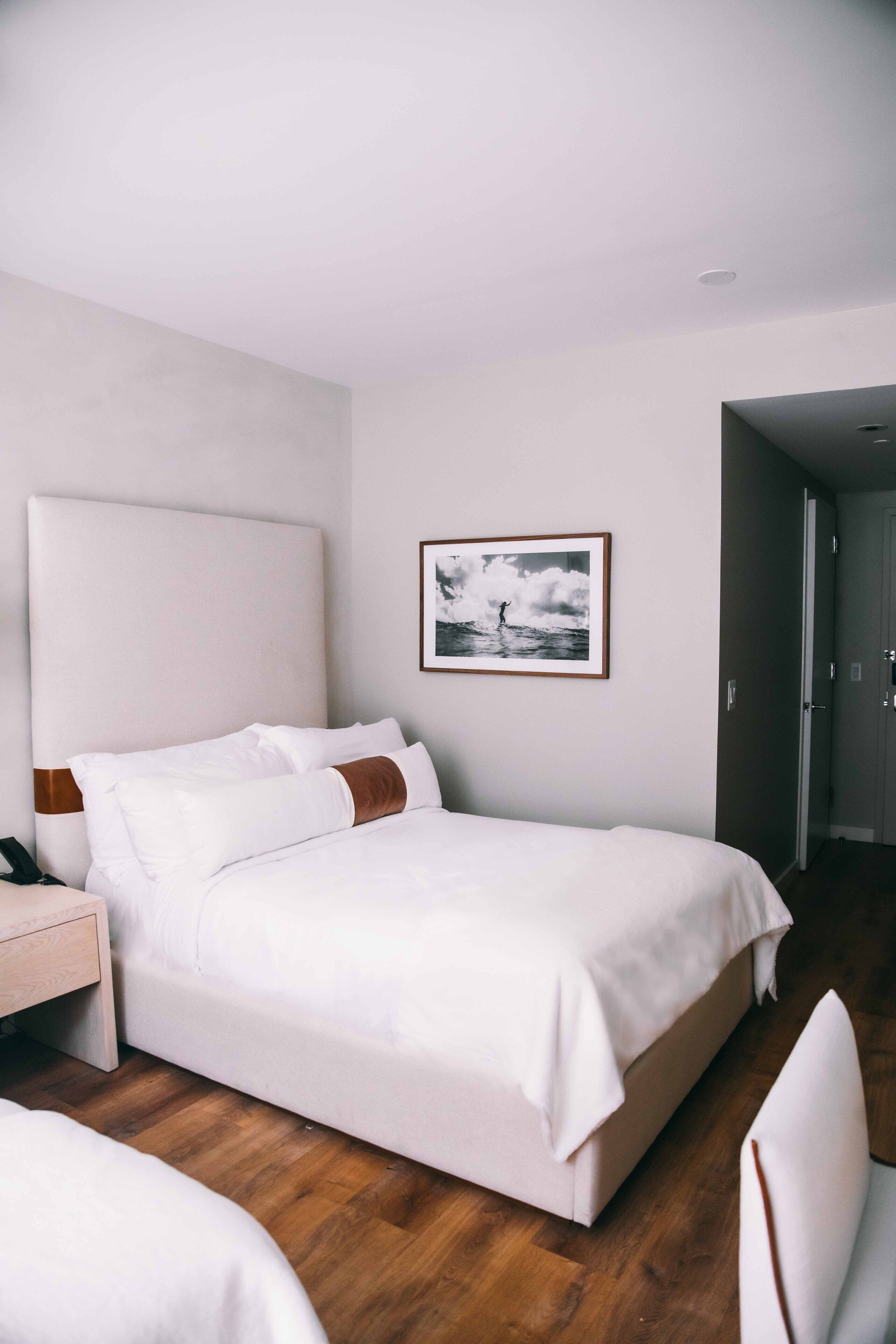 A neatly made bed with white linens and brown accents, a wooden nightstand, and a framed picture on the wall.
