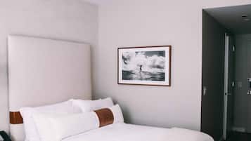 A neatly made bed with white linens and brown accents, a wooden nightstand, and a framed picture on the wall.
