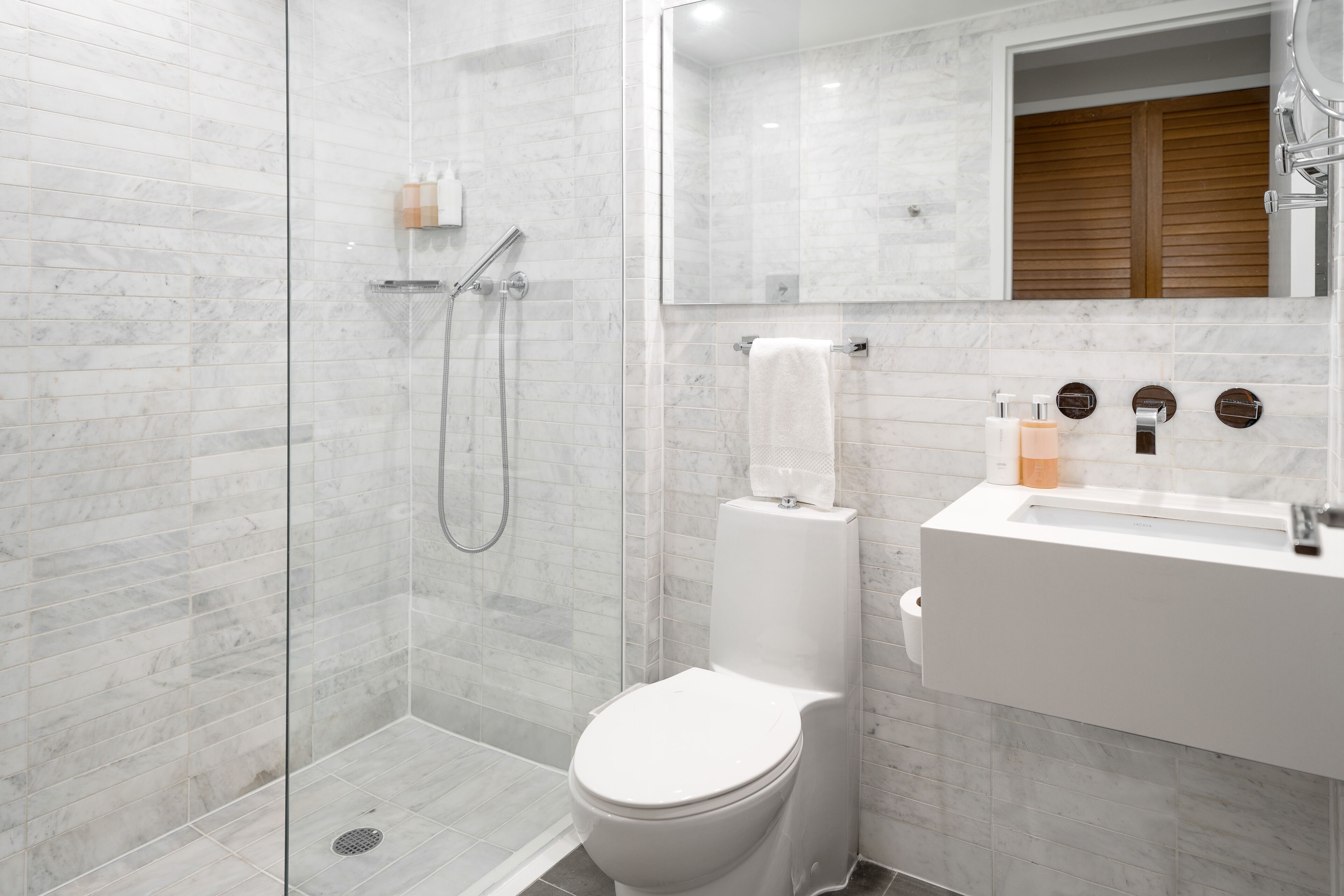 A modern bathroom with a glass-enclosed shower, a white toilet, and a sink with a mirror above it.