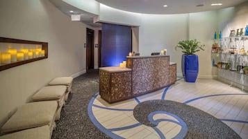A reception area with a reception desk, a seating area with cushioned benches, a decorative floor pattern, and a potted plant.